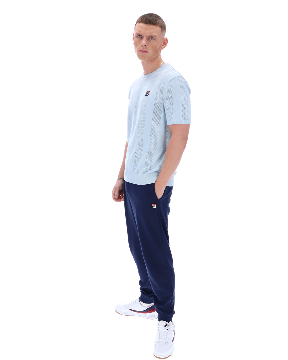 Man wearing a light blue t-shirt and navy tracksuit pants on a white background