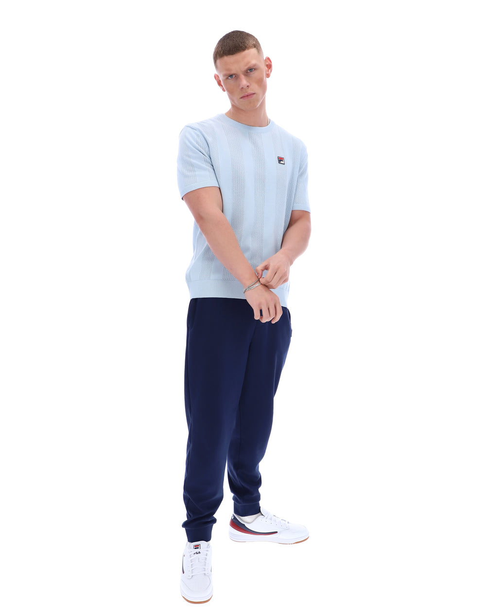 Man wearing a light blue t-shirt and navy tracksuit on a white background