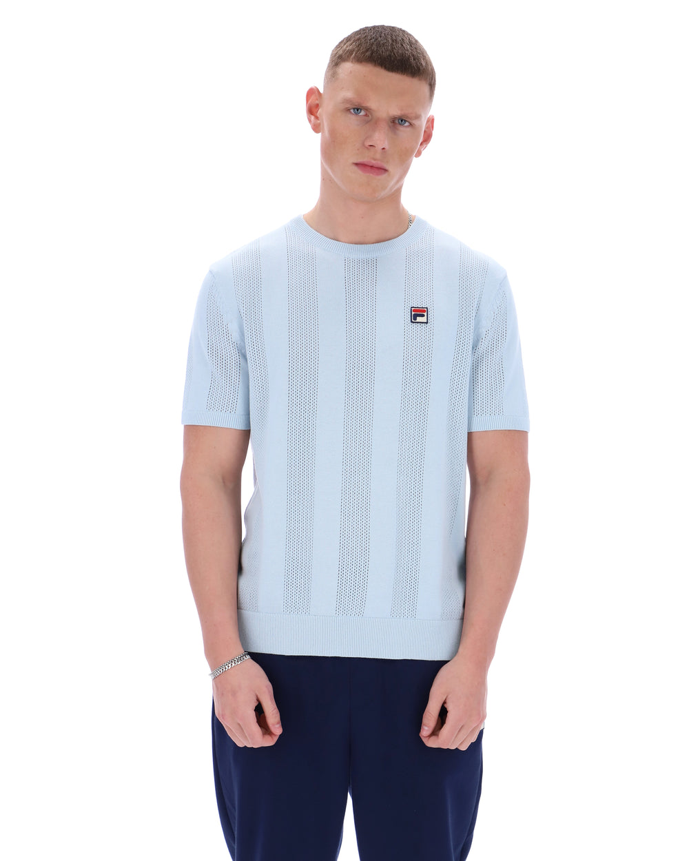 Man wearing a light blue textured t-shirt with a small logo on a white background