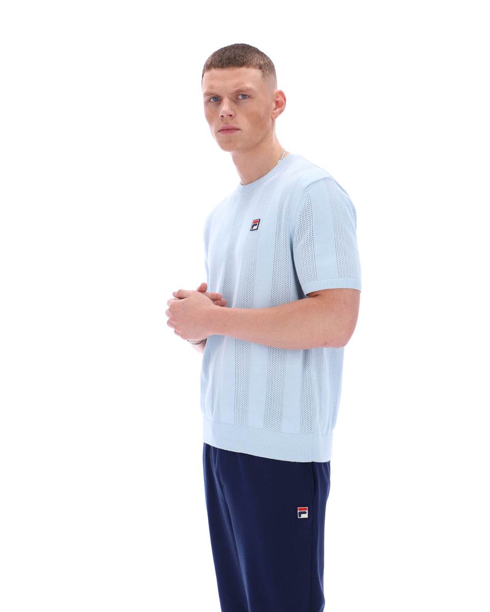 Man wearing a light blue t-shirt and navy shorts with a visible brand logo on a white background