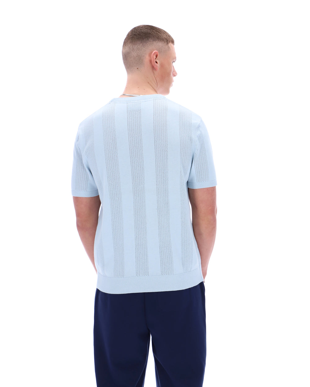 Man wearing a light blue ribbed sweater and navy pants on a white background