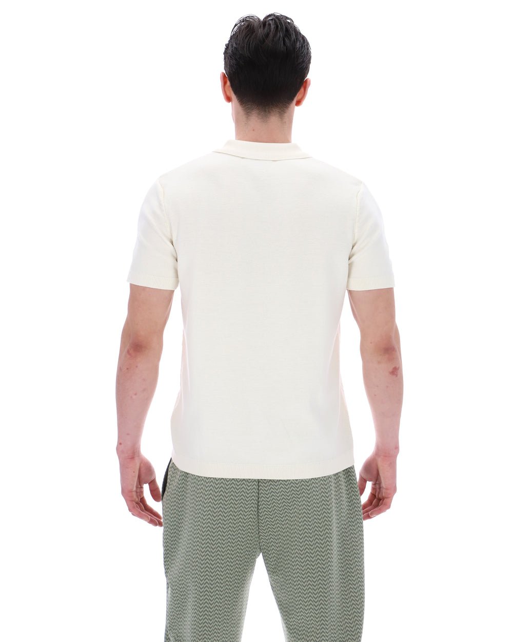 Person wearing a white polo shirt and green patterned pants on a white background