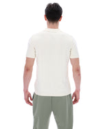 Person wearing a white polo shirt and green patterned pants on a white background