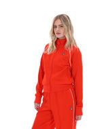 Woman wearing a bright orange tracksuit with white accents on a white background
