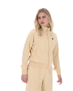 Woman wearing a beige track jacket with a FILA logo on the chest, paired with matching bottoms, against a white background