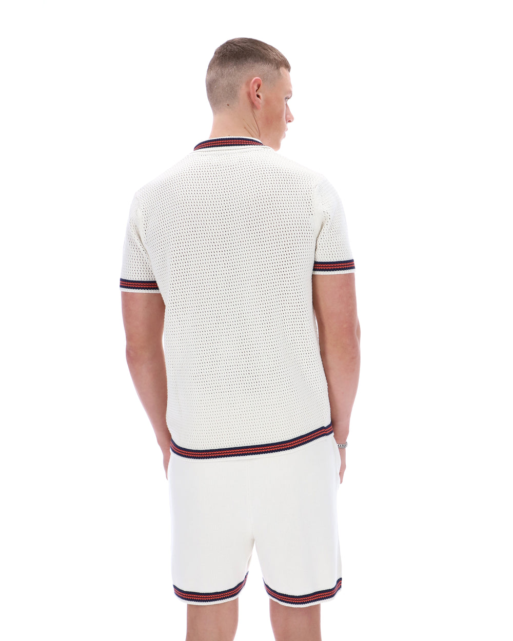 Man wearing a white textured polo shirt and shorts set with red and navy trim on a white background