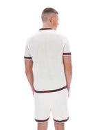 Man wearing a white textured polo shirt and shorts set with red and navy trim on a white background