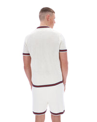 Man wearing a white textured polo shirt and shorts set with red and navy trim on a white background