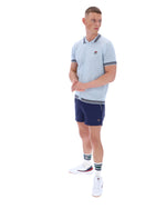 Man wearing a light blue patterned polo shirt with a FILA log on the chest and navy shorts, against a white background.