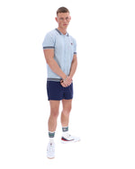 Man wearing a light blue patterned polo shirt with a FILA log on the chest and navy shorts, against a white background.