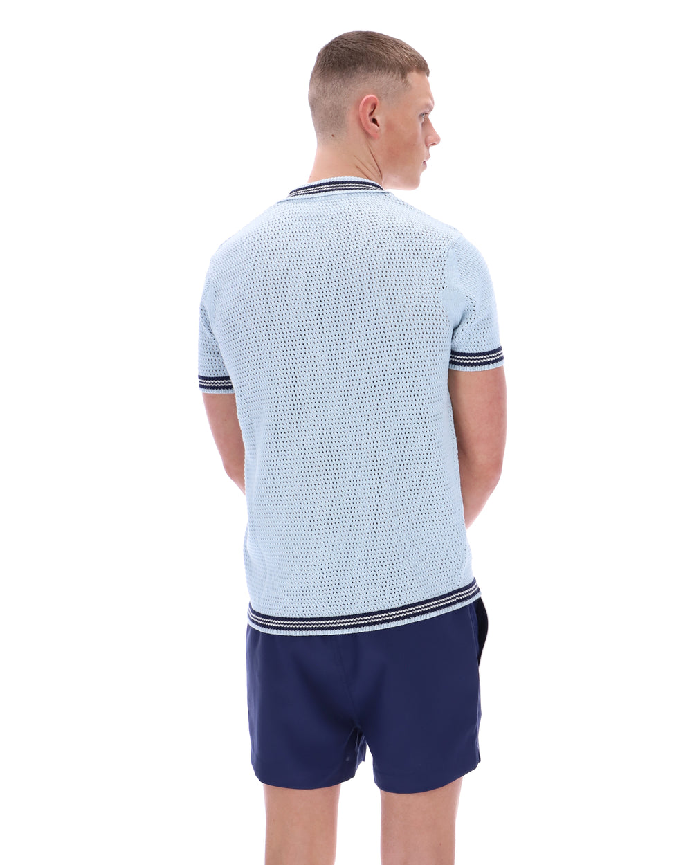 Man wearing a light blue textured polo shirt and navy shorts on a white background