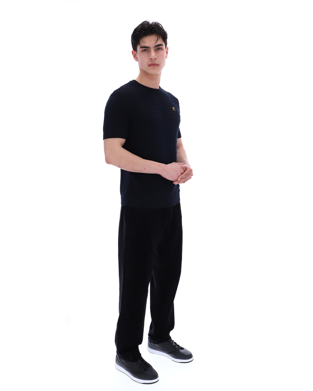 Man wearing a black t-shirt with a small FILA Gold logo on the chest with matching bottoms on a white background