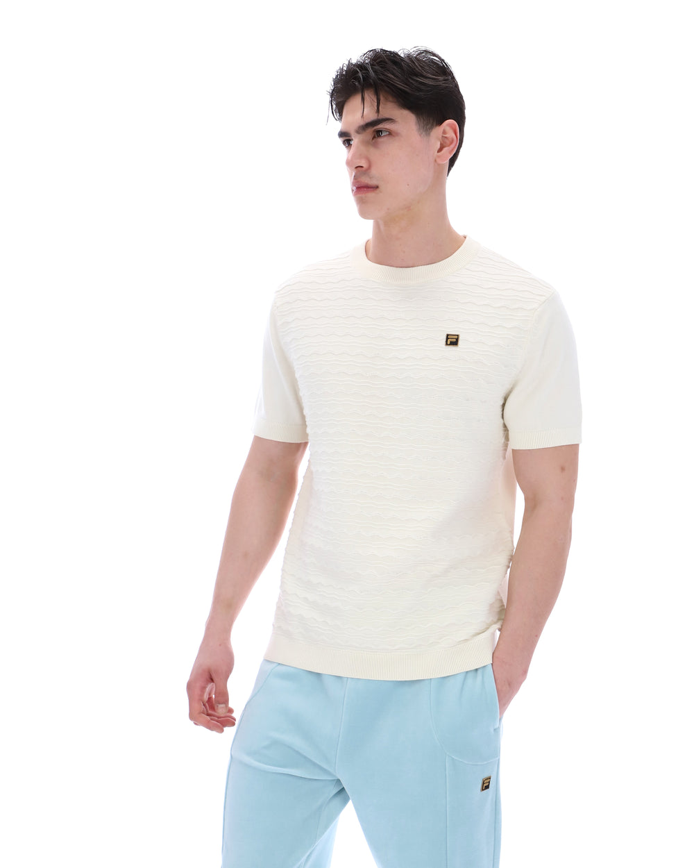 Man wearing a cream-coloured t-shirt and light blue pants on a white background