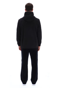 A man viewed from the back wearing a black hooded sweatshirt and black pants against a plain white studio background.