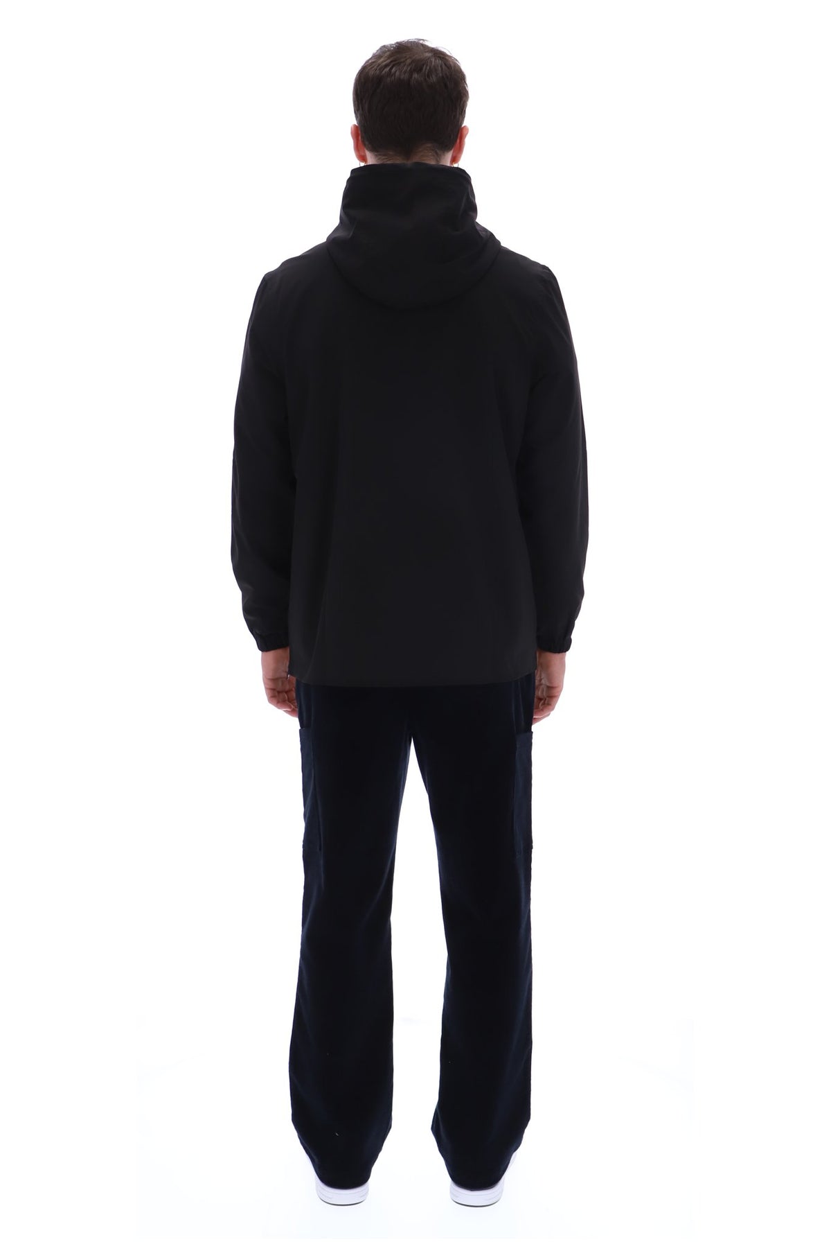 A man viewed from the back wearing a black hooded sweatshirt and black pants against a plain white studio background.