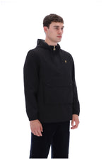 A man wearing a black hooded pullover jacket with a small gold embroidered logo on the left chest, paired with black pants, photographed against a solid white background.