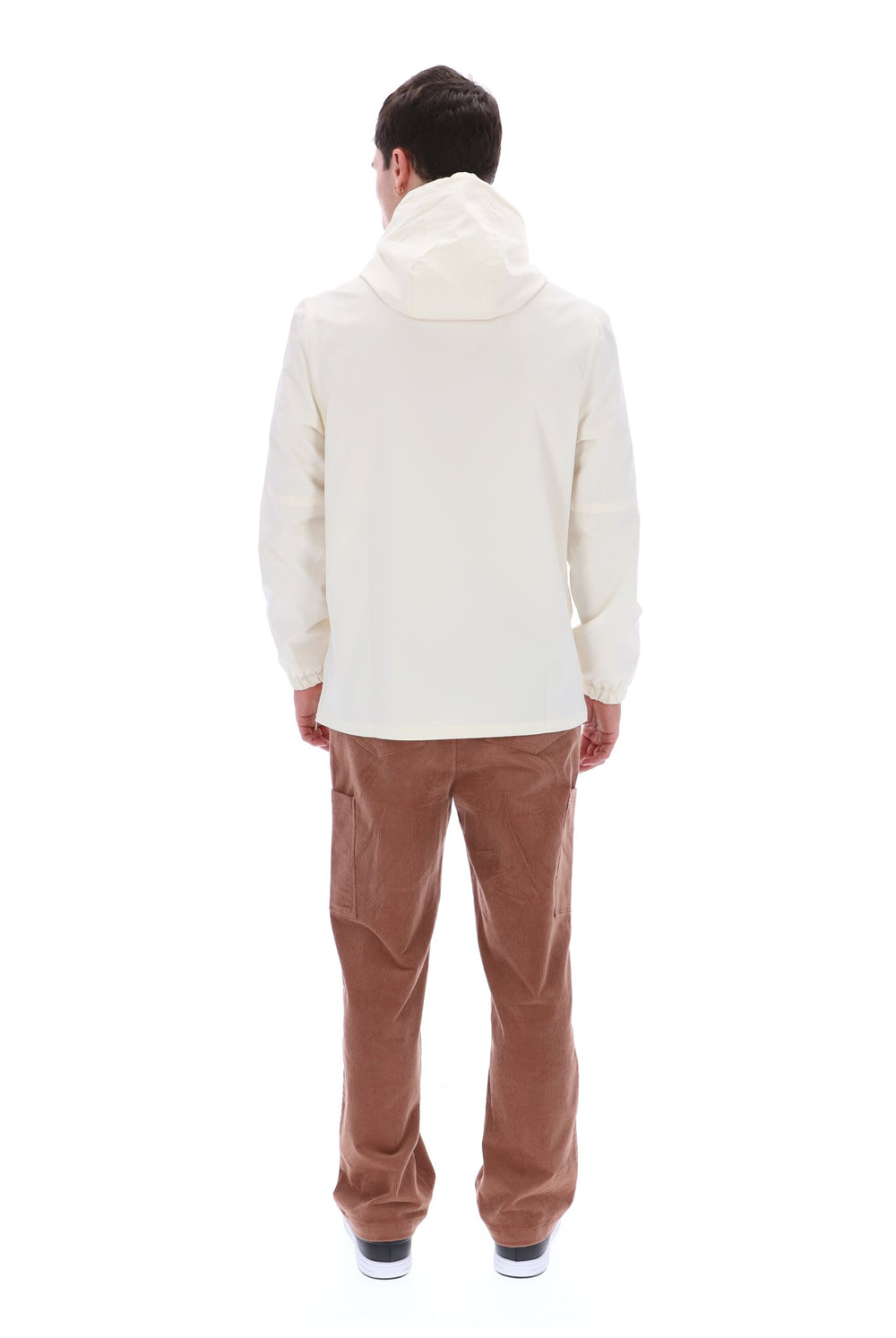 A man viewed from behind wearing a cream-colored hooded jacket and brown corduroy pants against a solid white background.