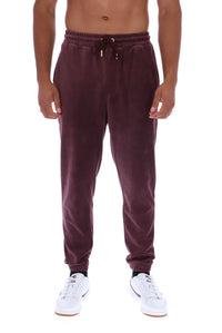 A man wearing dark plum corduroy jogger sweatpants with a drawstring waist and white sneakers, shown from the waist down against a plain white background.