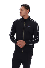 A man wearing a black Fila zip-up track jacket with white piping and a gold zipper, paired with matching black track pants, shot against a solid white background.