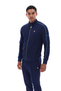 A man modeling a navy blue FILA tracksuit with light blue piping and a gold zipper, shot against a solid white background.