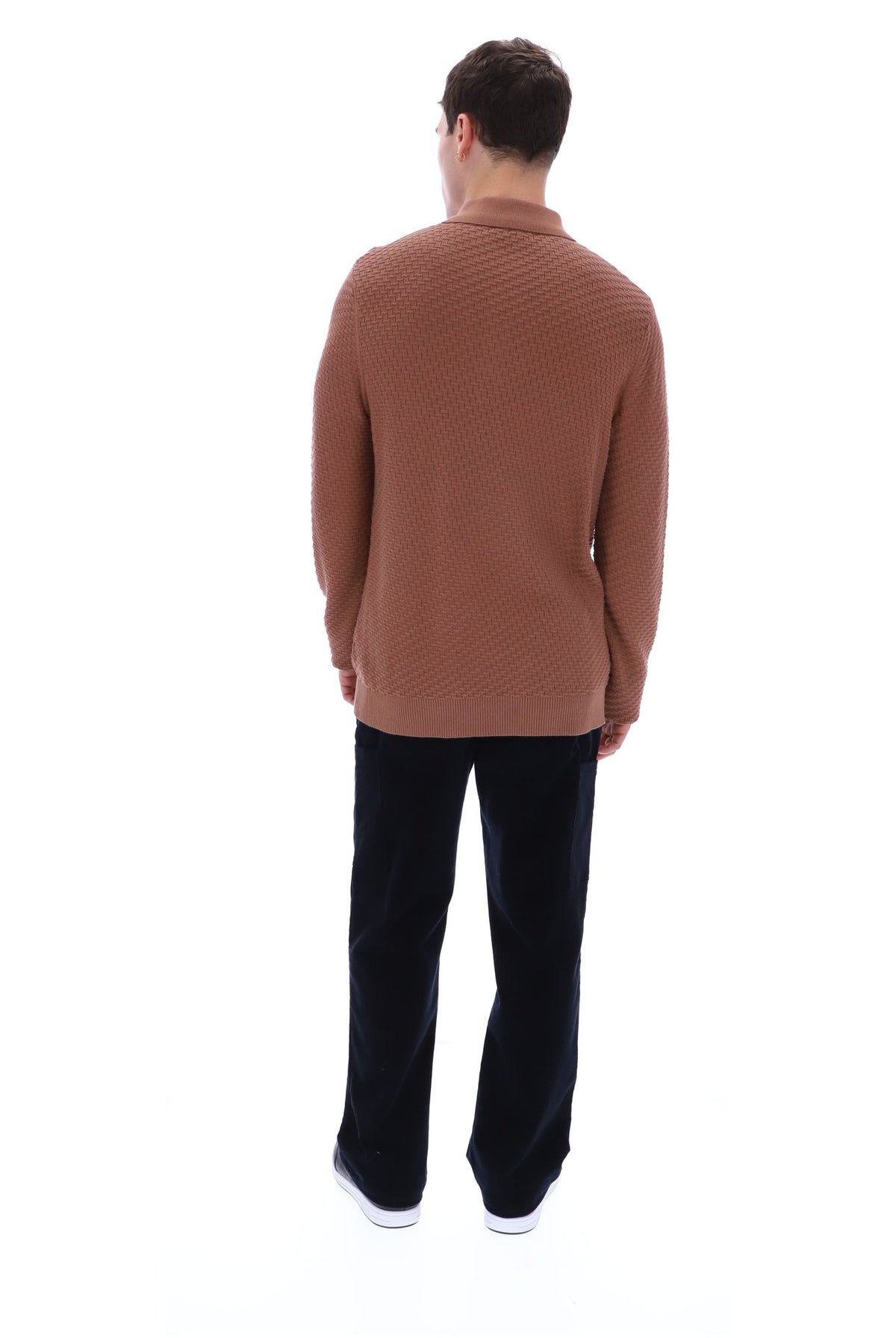 A man viewed from behind wearing a textured brown knit sweater and dark trousers, standing against a plain white background.
