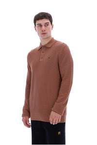 A man wearing a brown textured knit polo sweater with a small green embroidered logo on the chest, paired with black trousers, photographed against a solid white background.