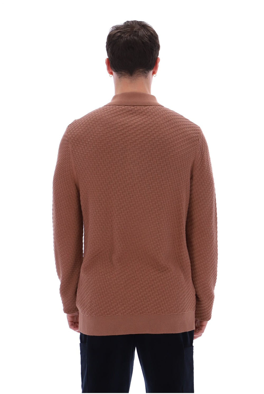 A man viewed from the back wearing a textured, waffle-knit brown sweater and dark trousers, set against a plain white background.