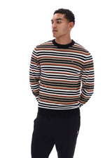 A man wearing a long-sleeve crewneck sweater with horizontal stripes in black, white, and tan, paired with black sweatpants, photographed against a solid white background.