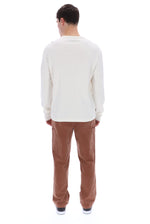 A man viewed from behind wearing a cream long-sleeve shirt and brown corduroy pants against a white background.