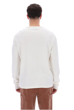 A man viewed from behind wearing a plain off-white long-sleeve crewneck shirt and brown pants, set against a solid white background.
