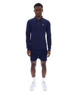 Man wearing a navy blue zip-up collared long-sleeve with a FILA logo on the chest, paired with matching shorts, on a white background