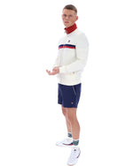 Man wearing a white sweater with red and blue accents and navy shorts on a white background