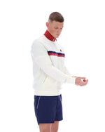 Man wearing a white jacket with red and blue accents and navy shorts on a white background