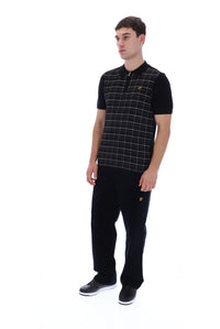 A man modeling a black short-sleeve polo shirt with a white windowpane grid pattern on the front, paired with black trousers and black sneakers, against a plain white background.