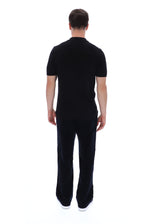 A man viewed from the back wearing a black short-sleeve polo shirt and matching black trousers, standing against a plain white studio background.