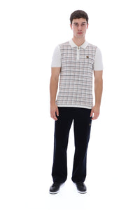 A man modeling a short-sleeve polo shirt with a beige and white plaid pattern on the body and white sleeves, paired with black trousers and black sneakers, against a solid white background.