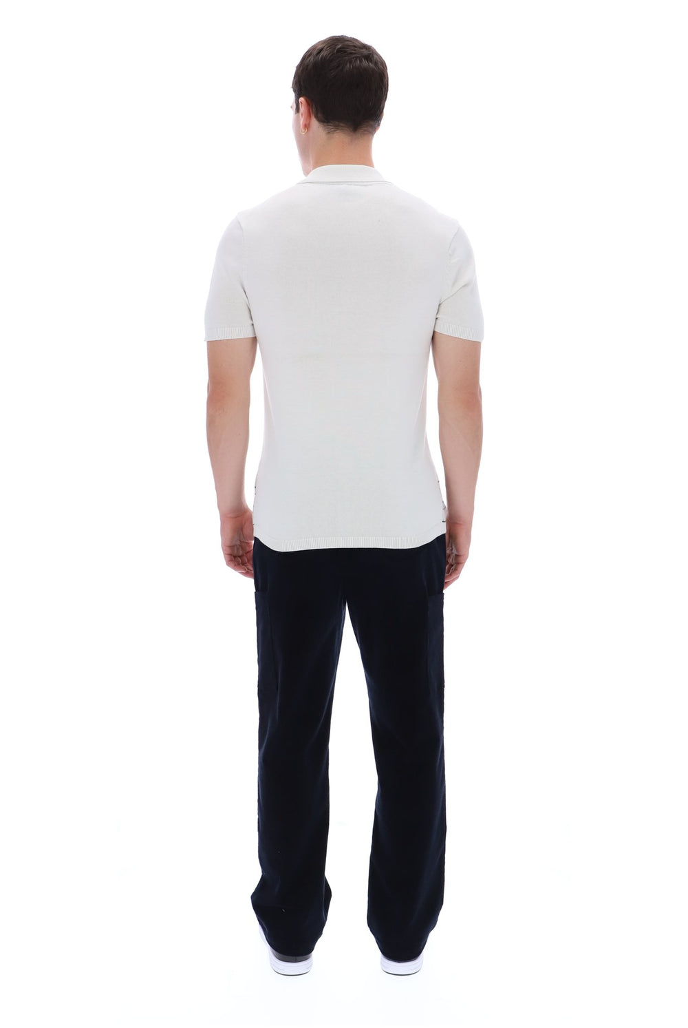 A man viewed from behind wearing a white short-sleeve polo shirt and dark navy trousers, standing against a plain white background.
