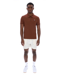 Man wearing a brown polo shirt and white shorts on a white background