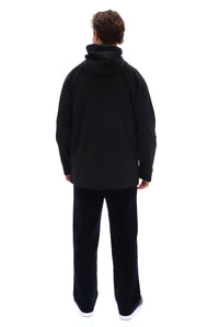 A man viewed from behind wearing a black hooded jacket and black pants against a plain white background.