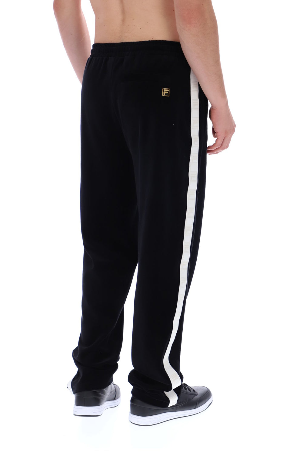 A man wearing black sweatpants with a prominent white side stripe and a small gold logo patch, shown from the back against a white background.