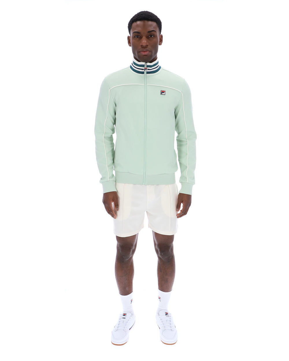 Man wearing a light green jacket with a FILA logo, white shorts, and white sneakers on a white background