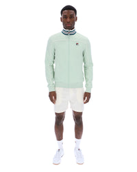 Man wearing a light green jacket with a FILA logo, white shorts, and white sneakers on a white background