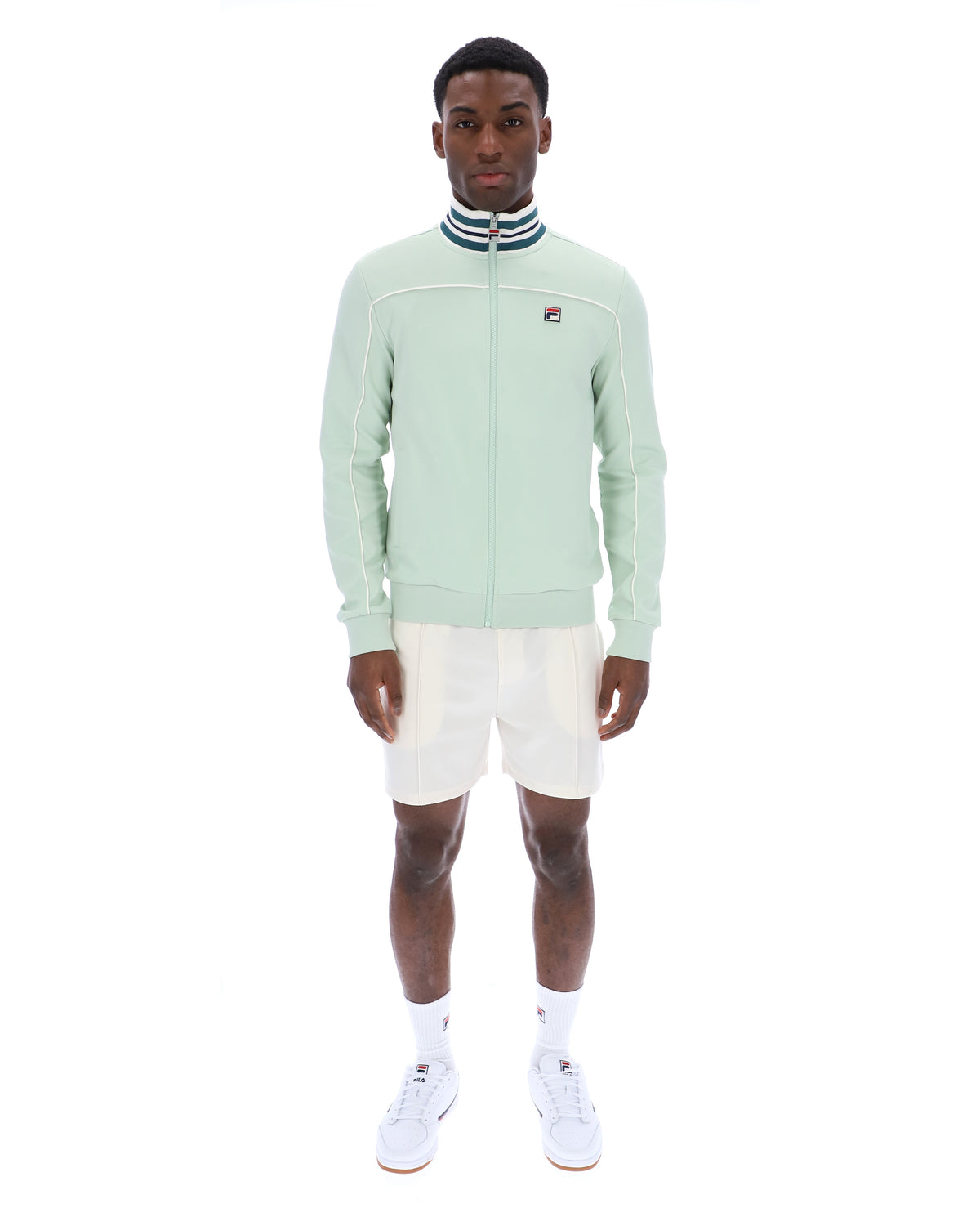 Man wearing a light green jacket with a FILA logo, white shorts, and white sneakers on a white background