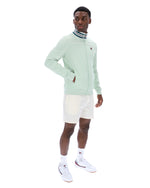 Man wearing a light green track jacket and white shorts on a white background