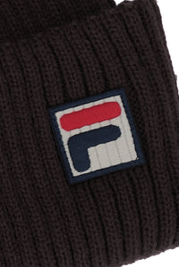 Close-up of a dark brown ribbed knit beanie featuring a square embroidered patch with the red, white, and navy blue FILA logo.