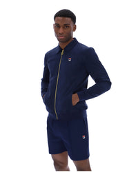 Man wearing a navy tracksuit jacket with a FILA logo on the chest, paired with matching shorts, on a white background