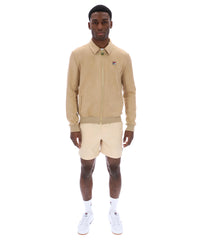 Man wearing a beige tracksuit Jacket with a small FILA logo on the chest, paired with cream shorts, on a white background