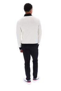 A man viewed from behind wearing a cream knit sweater with black ribbed trim, black trousers, and white sneakers with red accents, set against a plain white background.