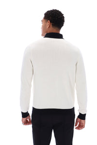 A man viewed from the back wearing a cream-colored knit sweater with black ribbed collar, cuffs, and hem, paired with black trousers, against a plain white background.