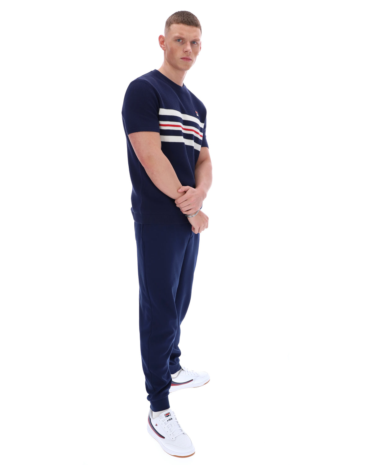 Man wearing a Navy blue t-shirt with white and red stripes and Fila logo with matching joggers on a white background